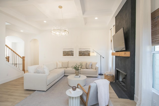 living room featuring a fireplace, coffered ceiling, light hardwood / wood-style flooring, a notable chandelier, and beamed ceiling