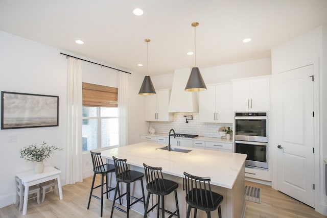 kitchen featuring appliances with stainless steel finishes, light stone counters, a kitchen island with sink, decorative light fixtures, and white cabinets