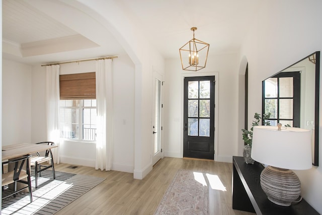 foyer entrance with a tray ceiling, a notable chandelier, and light wood-type flooring