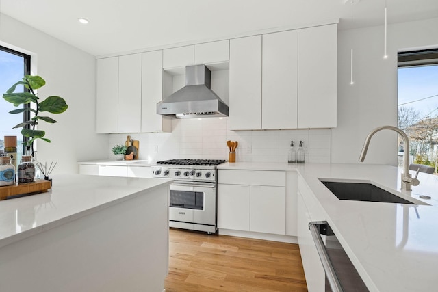 kitchen with high end stove, white cabinetry, sink, and wall chimney exhaust hood