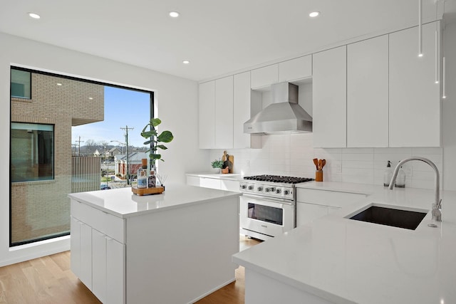 kitchen with white cabinetry, sink, high end stainless steel range oven, and wall chimney range hood