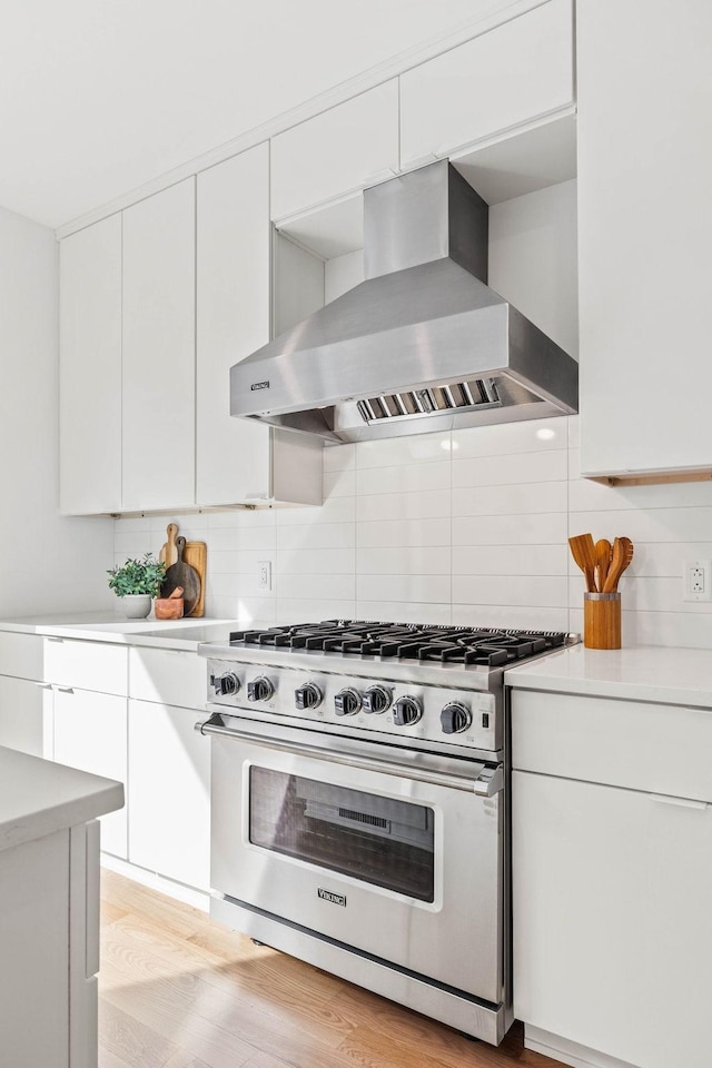 kitchen with white cabinets, light hardwood / wood-style flooring, wall chimney exhaust hood, decorative backsplash, and designer stove