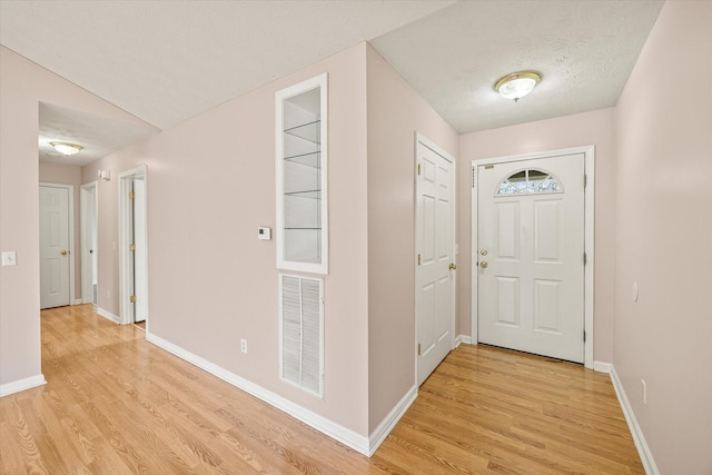 foyer entrance featuring a textured ceiling, light hardwood / wood-style floors, and lofted ceiling