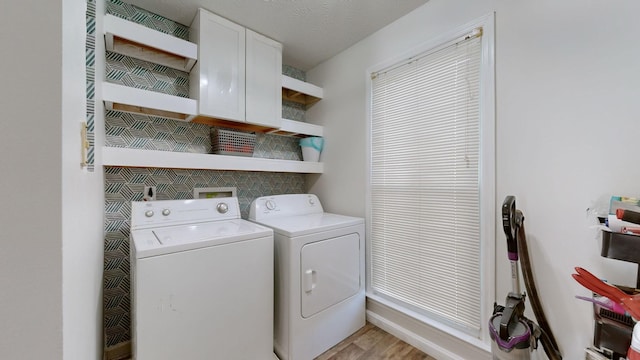 clothes washing area with washing machine and dryer, cabinets, a textured ceiling, and light hardwood / wood-style floors