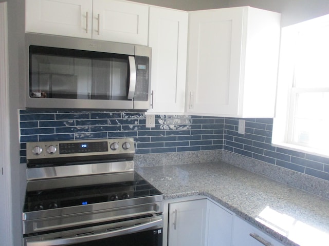 kitchen featuring decorative backsplash, white cabinets, stainless steel appliances, and light stone counters