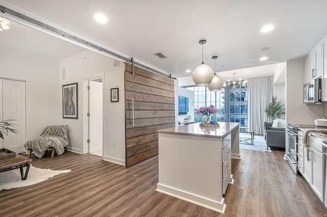 kitchen with pendant lighting, a barn door, a kitchen island, white cabinetry, and stainless steel appliances