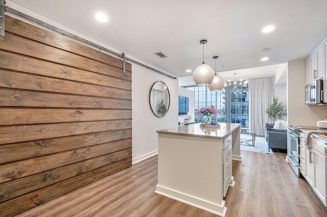 kitchen featuring stainless steel appliances, a barn door, white cabinets, a center island, and hanging light fixtures