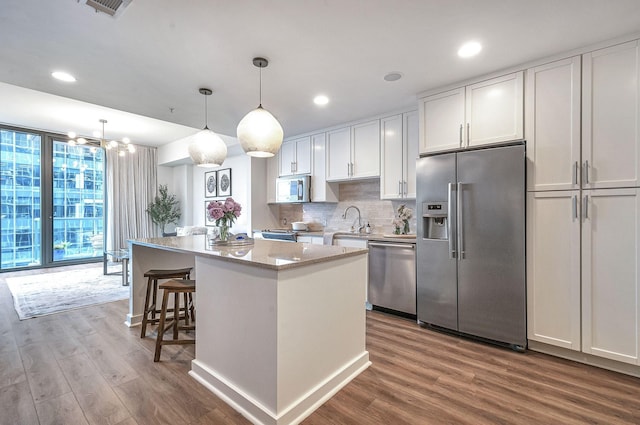 kitchen featuring appliances with stainless steel finishes, pendant lighting, white cabinets, hardwood / wood-style floors, and a kitchen island