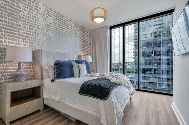 bedroom with wood-type flooring, expansive windows, and brick wall