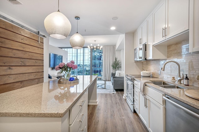 kitchen with white cabinets, a barn door, stainless steel appliances, and pendant lighting