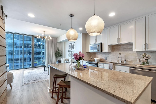 kitchen featuring tasteful backsplash, light hardwood / wood-style floors, decorative light fixtures, white cabinets, and appliances with stainless steel finishes