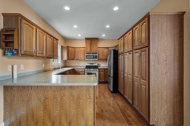 kitchen with kitchen peninsula, sink, stainless steel appliances, and wood-type flooring