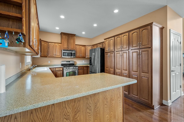 kitchen featuring kitchen peninsula, appliances with stainless steel finishes, light stone counters, sink, and hardwood / wood-style floors