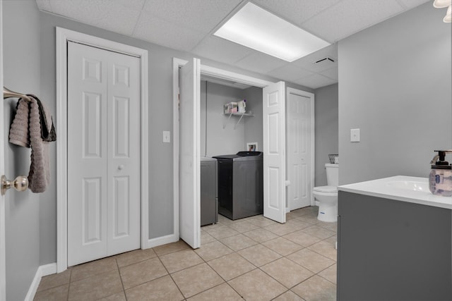 bathroom featuring a drop ceiling, vanity, washer and clothes dryer, tile patterned flooring, and toilet