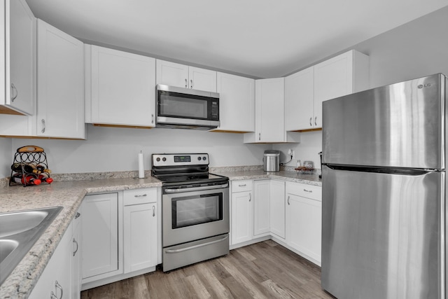 kitchen featuring white cabinets, sink, light stone countertops, light wood-type flooring, and appliances with stainless steel finishes