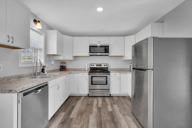 kitchen with white cabinets, light wood-type flooring, stainless steel appliances, and sink