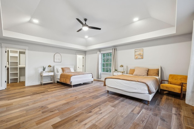 bedroom with a walk in closet, a tray ceiling, ceiling fan, and hardwood / wood-style flooring