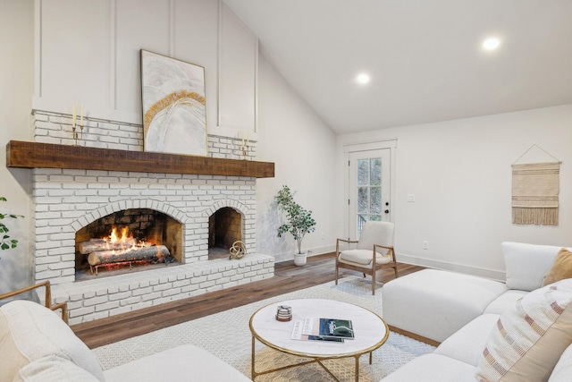 living room featuring hardwood / wood-style floors, lofted ceiling, and a brick fireplace