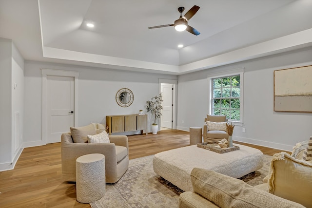 living room with light wood-type flooring, a tray ceiling, and ceiling fan