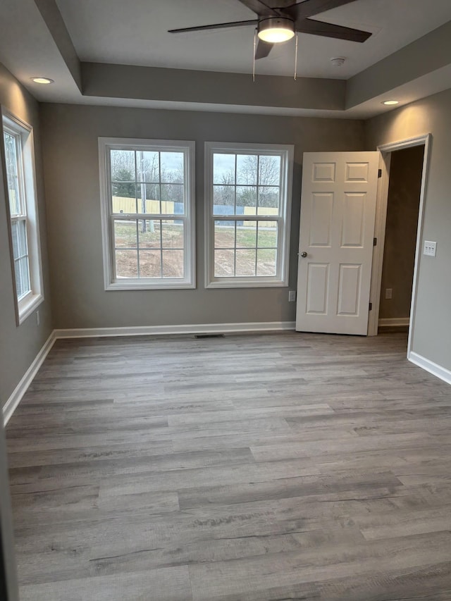 unfurnished room featuring light hardwood / wood-style floors, a raised ceiling, and ceiling fan