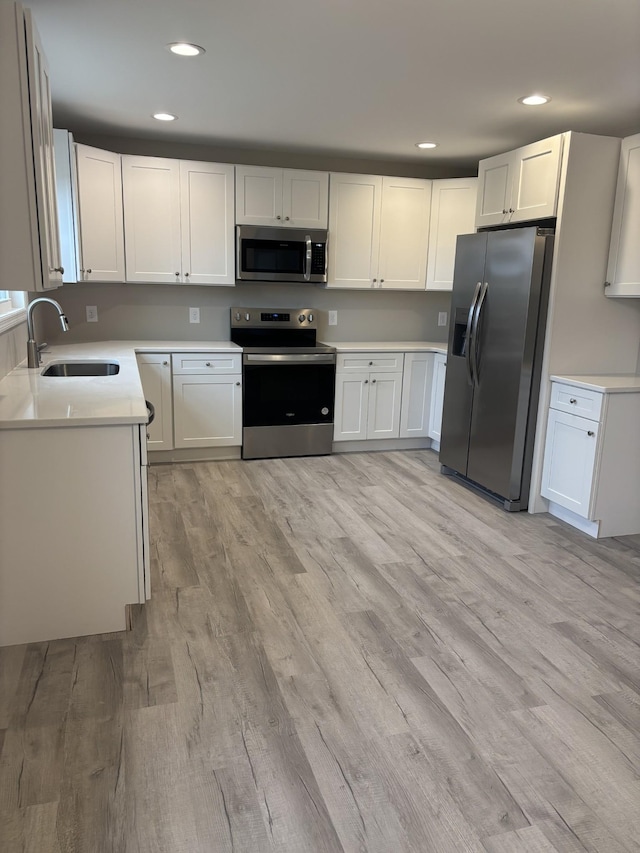 kitchen featuring sink, white cabinets, stainless steel appliances, and light wood-type flooring