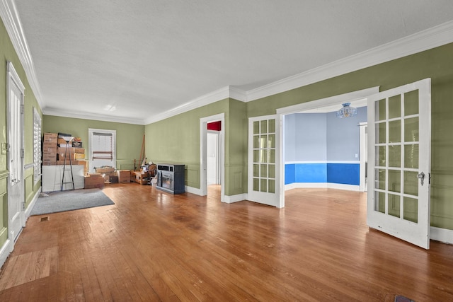 unfurnished living room featuring hardwood / wood-style floors, an inviting chandelier, french doors, and crown molding