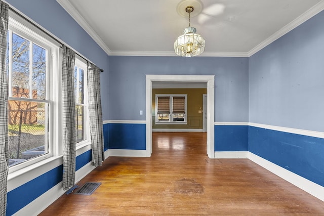 unfurnished dining area featuring wood-type flooring, an inviting chandelier, a wealth of natural light, and crown molding