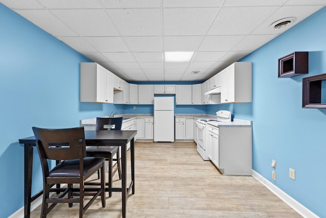 kitchen with white cabinetry, a drop ceiling, white appliances, and light wood-type flooring