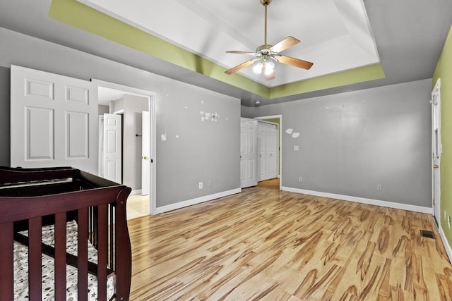 bedroom featuring light wood-type flooring, a tray ceiling, and ceiling fan