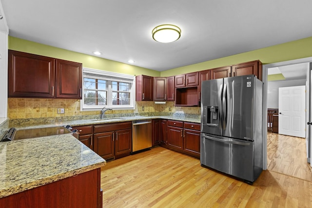 kitchen featuring backsplash, light stone counters, stainless steel appliances, sink, and light hardwood / wood-style flooring