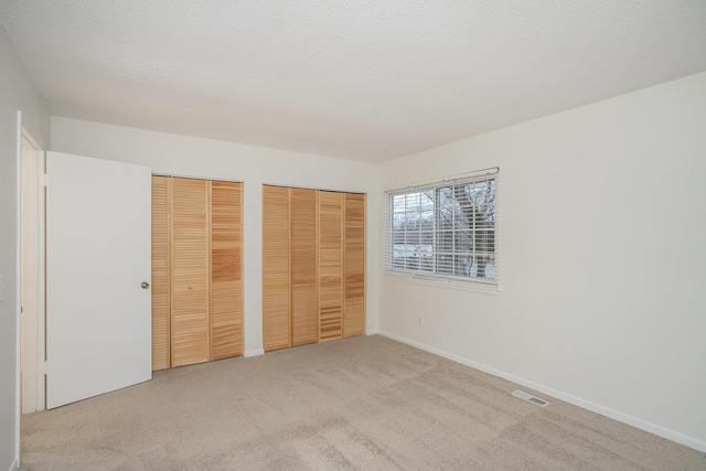 unfurnished bedroom with light colored carpet, a textured ceiling, and multiple closets