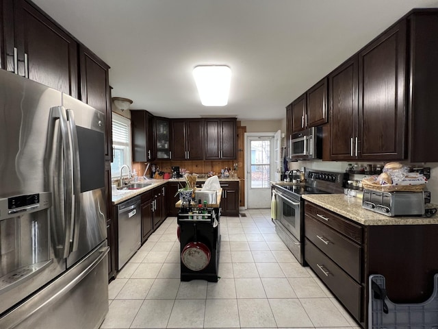 kitchen with sink, stainless steel appliances, a kitchen island, dark brown cabinets, and light tile patterned floors