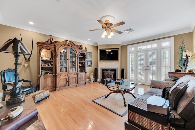 living room with a tile fireplace, ceiling fan, hardwood / wood-style floors, and crown molding