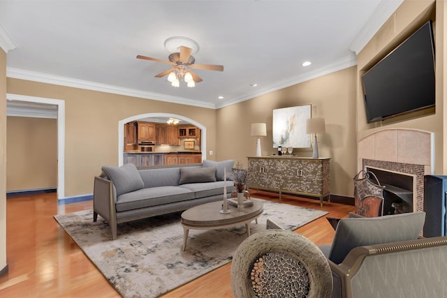 living room featuring ceiling fan, a fireplace, light hardwood / wood-style floors, and ornamental molding