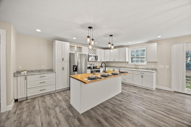 kitchen with white cabinetry, a center island with sink, wooden counters, and appliances with stainless steel finishes