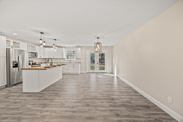 kitchen with white cabinetry, decorative light fixtures, a kitchen island, butcher block counters, and stainless steel appliances