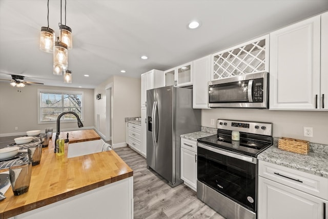 kitchen featuring white cabinetry, sink, butcher block countertops, decorative light fixtures, and appliances with stainless steel finishes