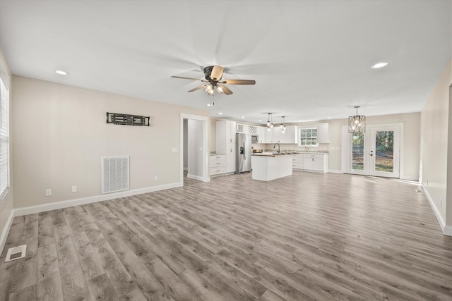 unfurnished living room with ceiling fan with notable chandelier, french doors, light wood-type flooring, and sink