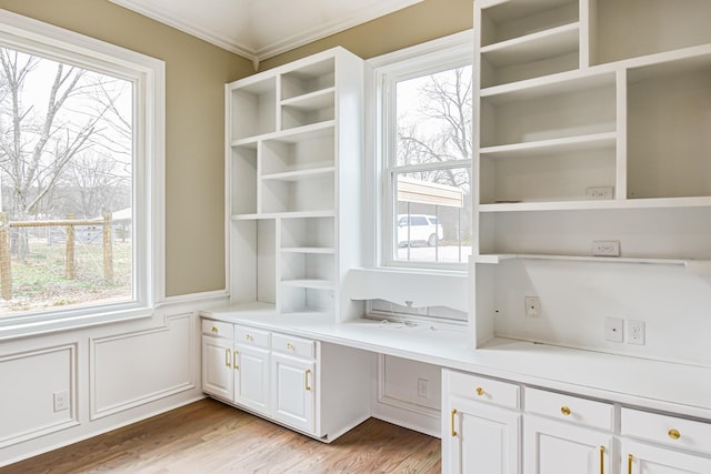 unfurnished office with a healthy amount of sunlight, built in desk, ornamental molding, and light hardwood / wood-style flooring