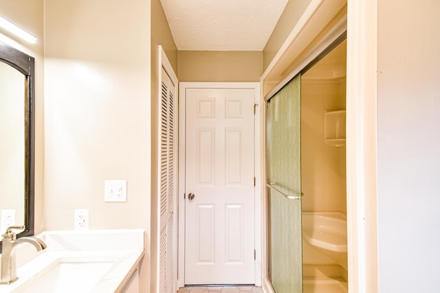 bathroom with tile patterned flooring, vanity, a shower with door, and a textured ceiling