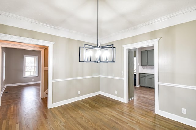 unfurnished dining area with dark hardwood / wood-style floors, crown molding, and a chandelier