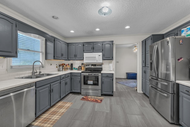 kitchen featuring gray cabinetry, sink, backsplash, appliances with stainless steel finishes, and ornamental molding