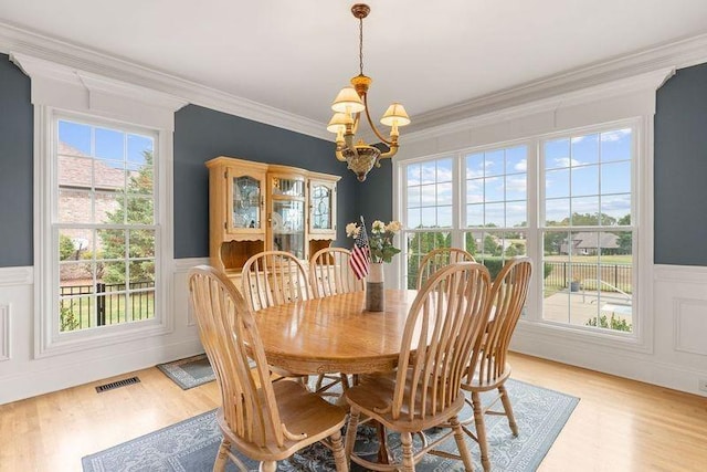 dining space featuring light wood-type flooring, ornamental molding, and a notable chandelier