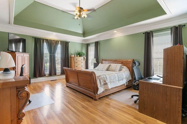 bedroom featuring a tray ceiling, light hardwood / wood-style flooring, ceiling fan, and ornamental molding