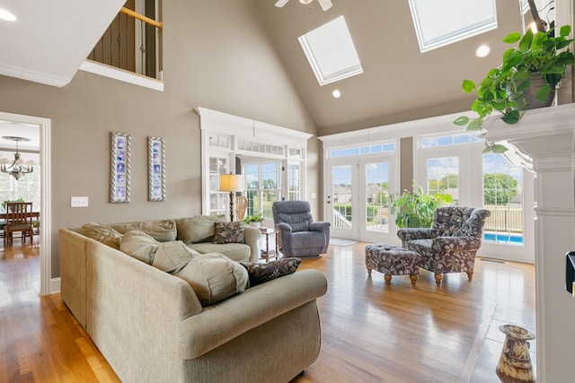 living room with high vaulted ceiling, french doors, ceiling fan with notable chandelier, a skylight, and light hardwood / wood-style floors