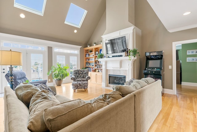 living room with a skylight, ornamental molding, high vaulted ceiling, light hardwood / wood-style floors, and a tiled fireplace