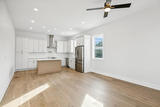 kitchen with a center island, backsplash, white cabinets, wall chimney exhaust hood, and stainless steel appliances