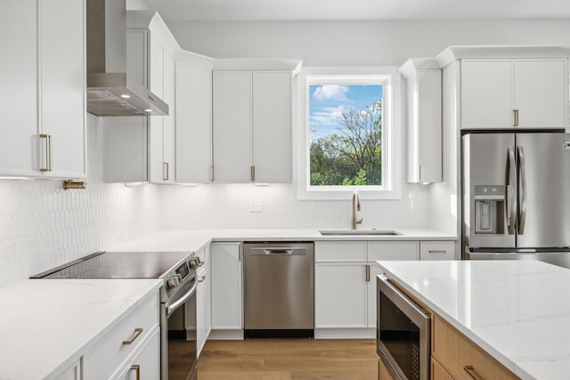 kitchen with white cabinets, wall chimney range hood, sink, light stone counters, and stainless steel appliances