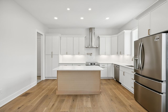 kitchen featuring light wood-type flooring, wall chimney exhaust hood, stainless steel appliances, a center island, and white cabinetry