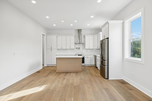 kitchen featuring wall chimney exhaust hood, tasteful backsplash, a kitchen island, white cabinetry, and stainless steel appliances